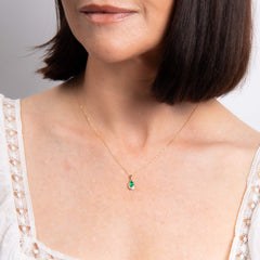 A close-up of a woman's neck wearing the emerald teardrop pendant on a delicate gold chain.