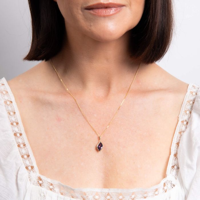 Woman wearing a delicate gold necklace with a small pendant against a neutral background