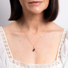 Woman wearing a delicate gold necklace with a small pendant against a neutral background