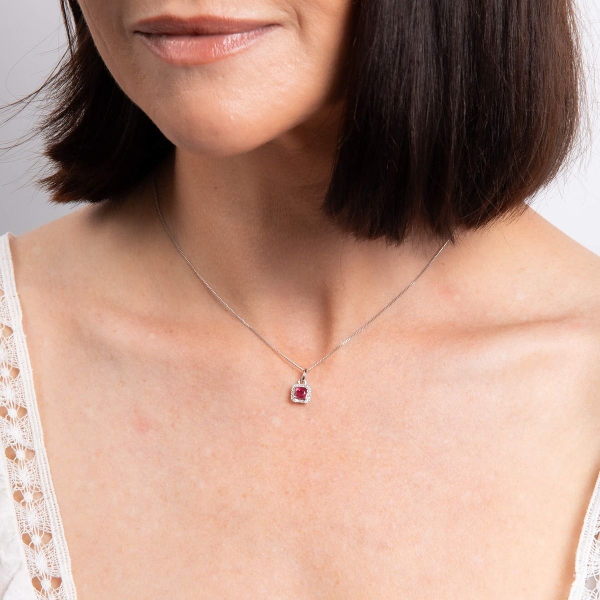 Close-up of a woman wearing a silver necklace with a red gemstone pendant.