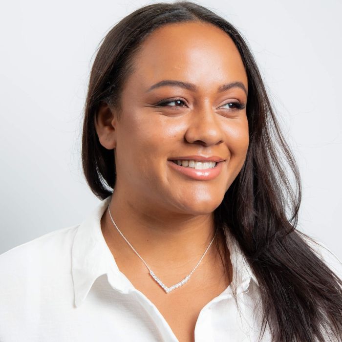 Woman wearing a white shirt and necklace against a plain background