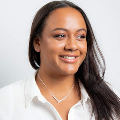 Woman wearing a white shirt and necklace against a plain background