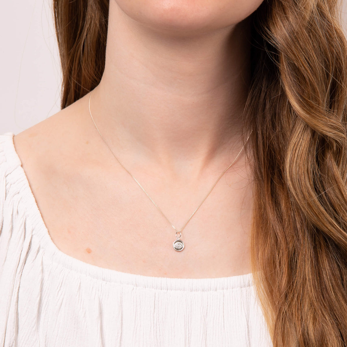 Evil eye charm pendant in recycled silver worn as a necklace on model