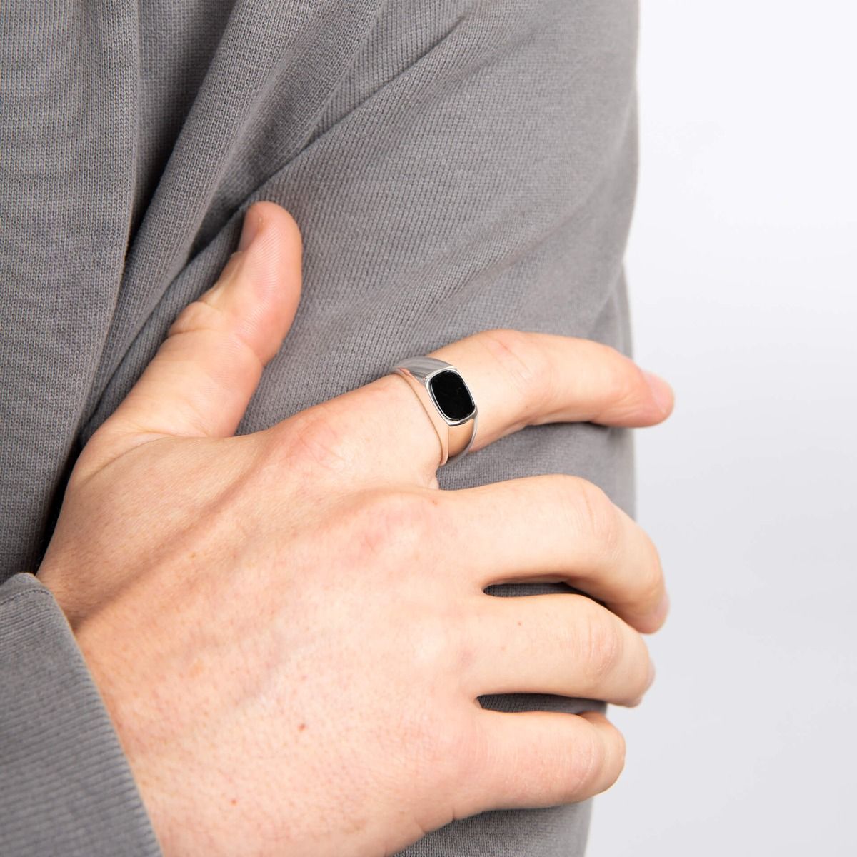 A close-up of a man wearing a silver and black onyx signet ring on his pinky finger, resting his hand on his shoulder.