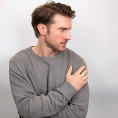 A man wearing a silver oval signet ring on his ring finger, looking to the side with his hand on his chest.