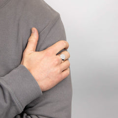 A man wearing a silver oval signet ring on his ring finger, with his hand resting on his arm.