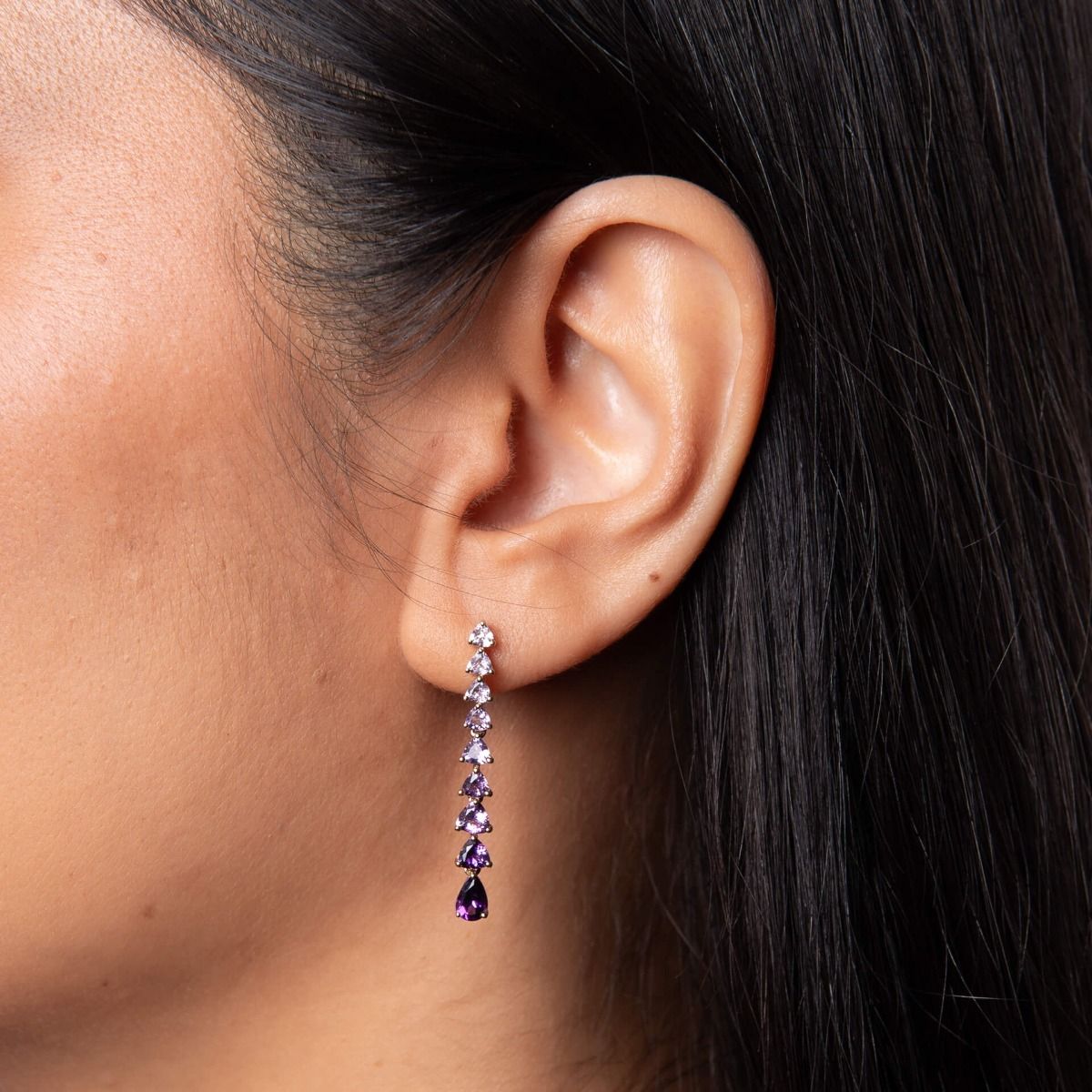 A close-up of a woman's ear wearing the 9ct gold cascading amethyst drop earrings from the set.