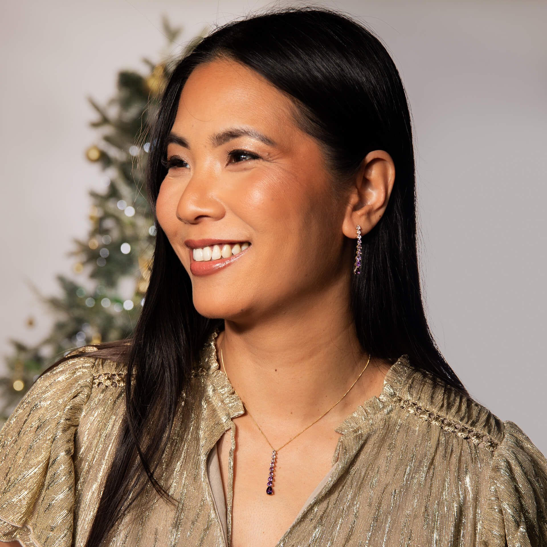 Woman wearing a gold glittery top with a Christmas tree in the background