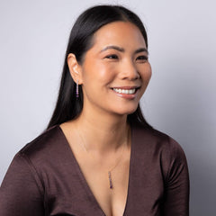 A smiling woman wearing a gold amethyst pendant necklace and matching drop earrings, dressed in a gold top with a Christmas tree in the background.